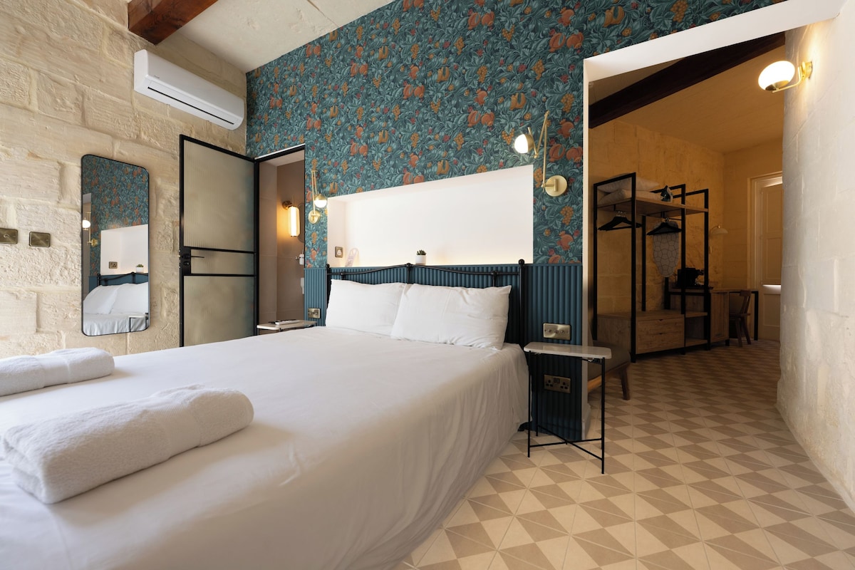 A hotel room with a large bed, a mirror, a wardrobe, and a bathroom visible through an open door.