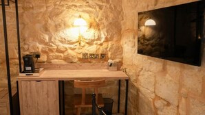 A cozy, stone-walled room with a wooden desk, a chair, and a mounted TV. - Fourteen Guesthouse  (Żejtun)