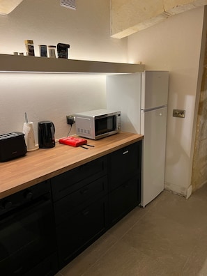 A compact kitchen with a microwave, toaster, and a small refrigerator. - Fourteen Guesthouse (Żejtun)