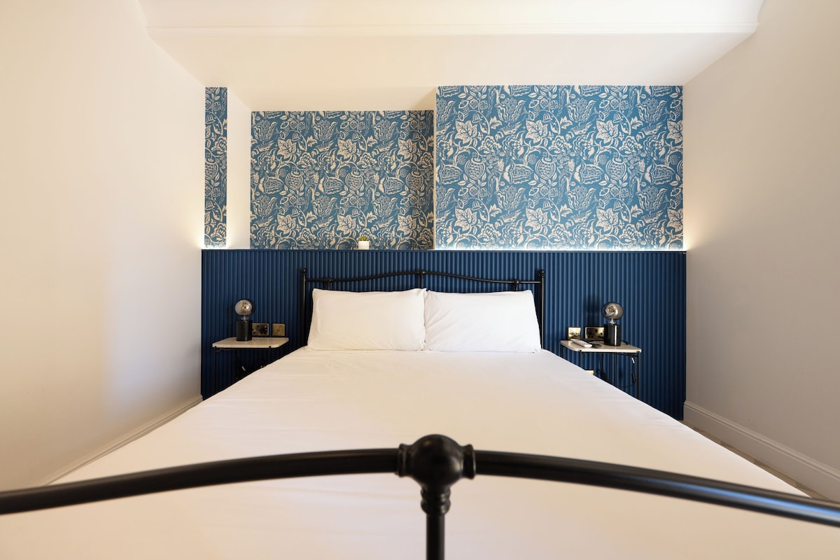 A hotel room with a large bed, two bedside tables, and a headboard with a blue patterned wallpaper.