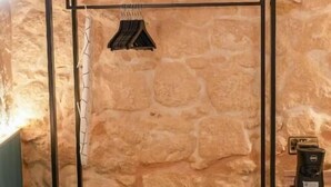 A room with a stone wall, a wooden bed frame, a small wooden table with a coffee maker, and a shelf with an iron. - Fourteen Guesthouse  (Żejtun)