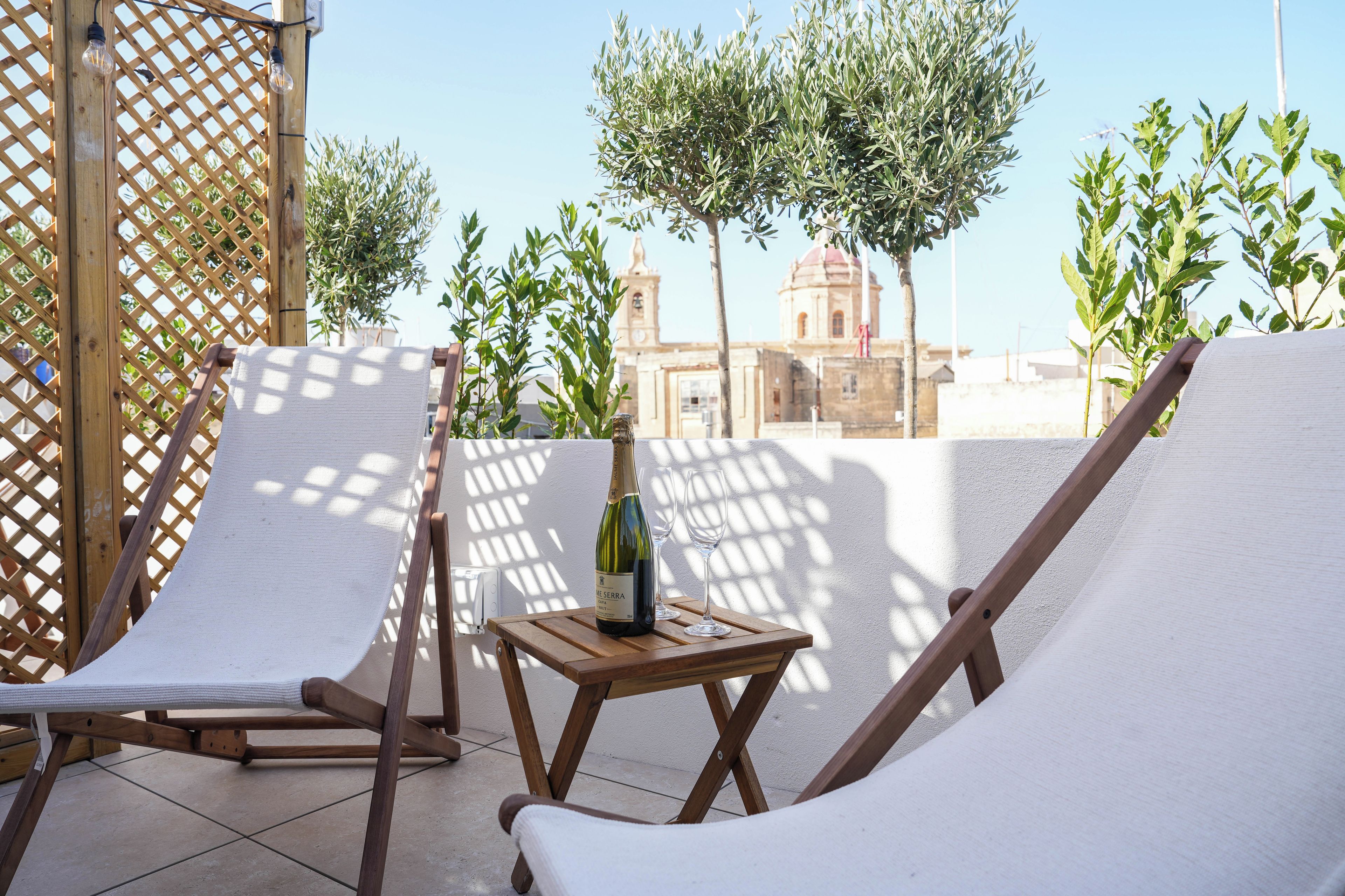 A terrace with two lounge chairs, a bottle of wine, and a glass on a small wooden table.