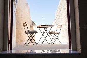 A narrow outdoor space with a table and two chairs, enclosed by walls. - Fourteen Guesthouse (Żejtun)