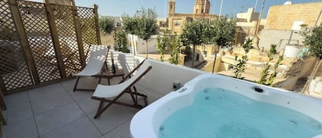 Una terraza en la azotea con un jacuzzi, sillones de descanso y vistas a un edificio histórico.