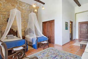 Un dormitorio con dos camas, una pared de piedra, puertas de madera y una alfombra colorida.