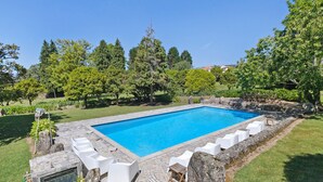 Una piscina rectangular con borde de piedra y sillones reclinables blancos alrededor.