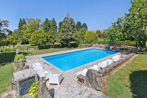 Una piscina rectangular con borde de piedra y sillones reclinables blancos alrededor.