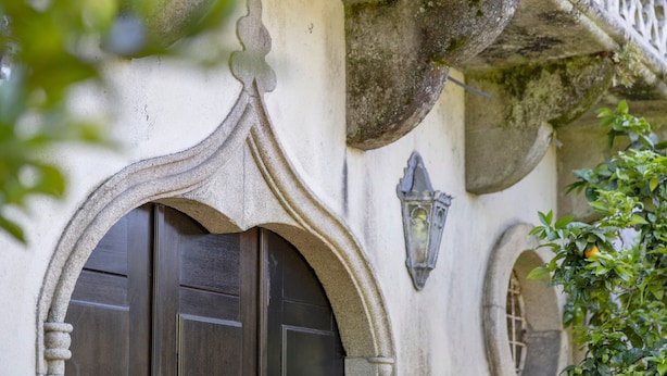 Ein Steinhaus mit einer dunklen Holztür, einem steinernen Bogen und einem kleinen Fenster mit Gitterwerk.