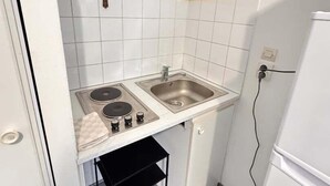 A compact kitchen with white tiles, a double sink, a small countertop, and a black metal shelf. - Little Arras — 25 m² apartment in Arras center (Arras)