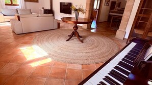 Un saló amb un piano, un sofà, una televisió i una zona de menjador amb taula i cadires.