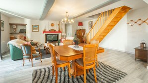 A dining area with a wooden table and chairs, a fireplace, and a staircase.