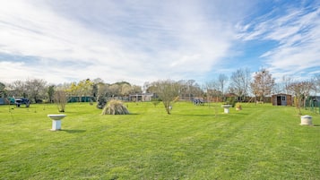 Un vaste espace extérieur doté d’une pelouse bien entretenue, de quelques arbres dispersés et d’un petit bâtiment visible au loin.