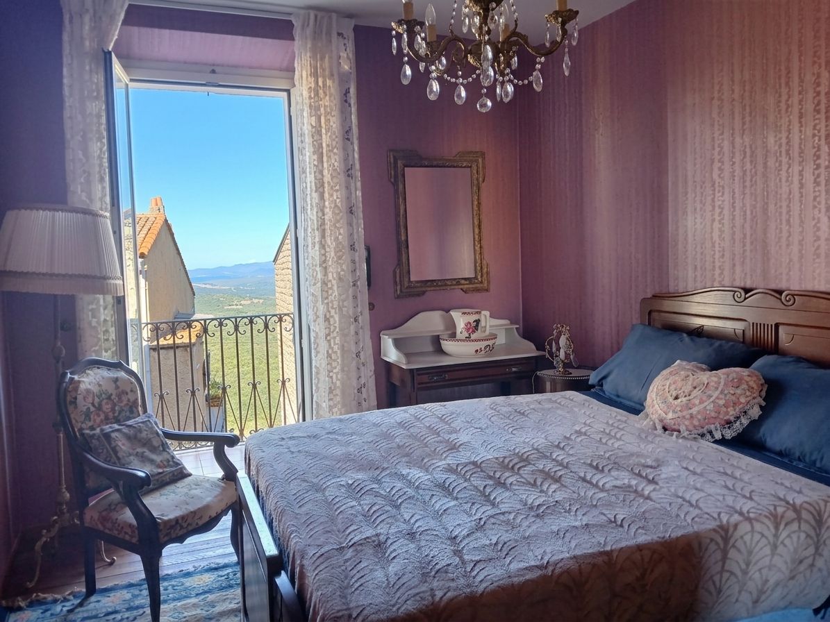 Ein Schlafzimmer mit einem großen Bett, einem Sessel, einer Kommode und Blick ins Freie.