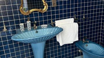 Une salle de bain avec un mur recouvert de carreaux bleus, un grand miroir avec un cadre doré, un lavabo sur colonne, un bidet et un porte-serviettes.
