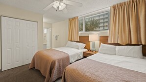 A hotel room with two beds, a ceiling fan, a window with curtains, and a view of a building outside. - Easy Oceanfront Escape | 1BR Sleeps 6 Ormond Beach (Ormond Beach)