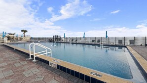 Una piscina con un cartello che vieta tuffi, sedie a sdraio e vista sulla spiaggia.