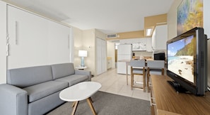 A compact living space with a sofa, a small table, a television, and a kitchenette. - Ocean View Resort w/ Beachfront Pool & Beach Access - Studio (Ormond Beach)