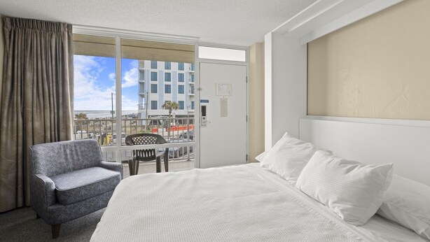Camera d'albergo con un letto, una sedia e vista su un edificio e una spiaggia.