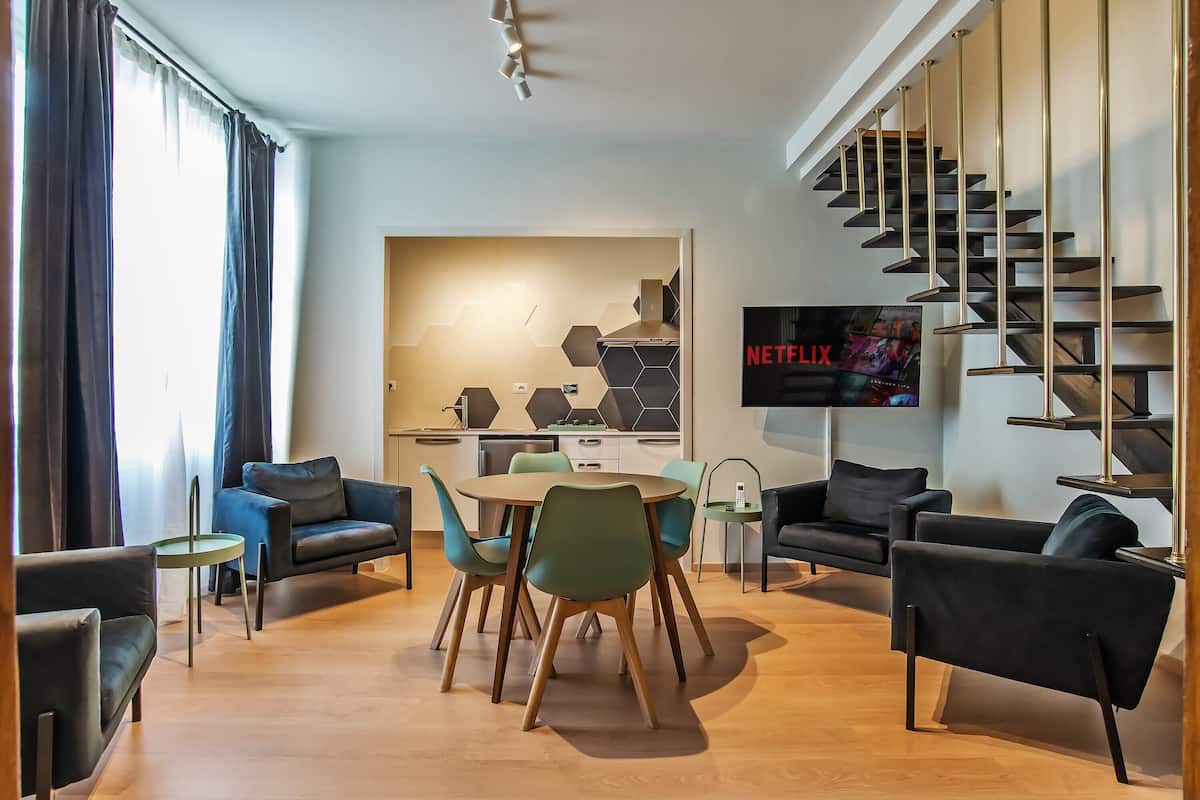 A modern living room with a dining area, a kitchen, and a staircase.