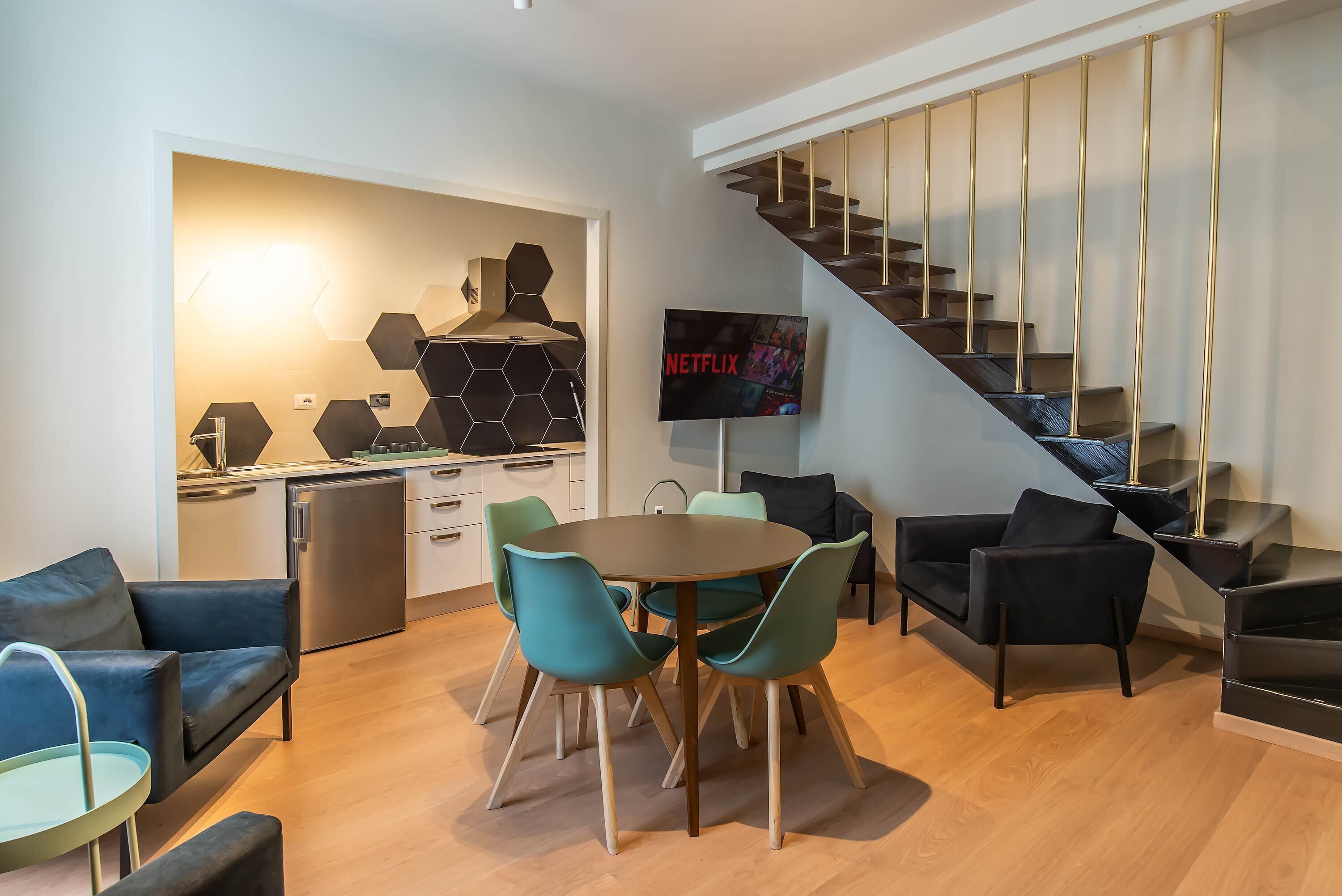 A modern living area with a dining table, chairs, sofas, a TV, and a staircase.