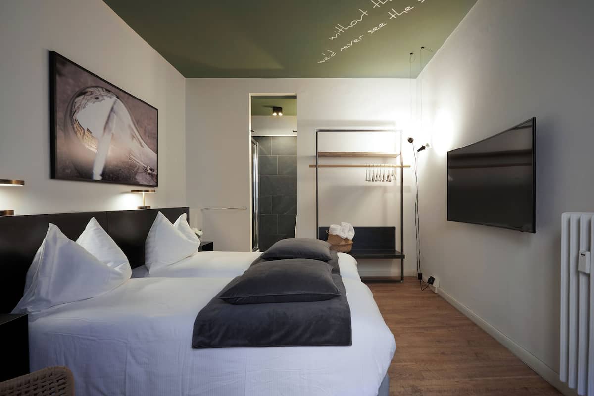 A modern hotel room with a large bed, a flat-screen TV, a painting, and a view of a cityscape.