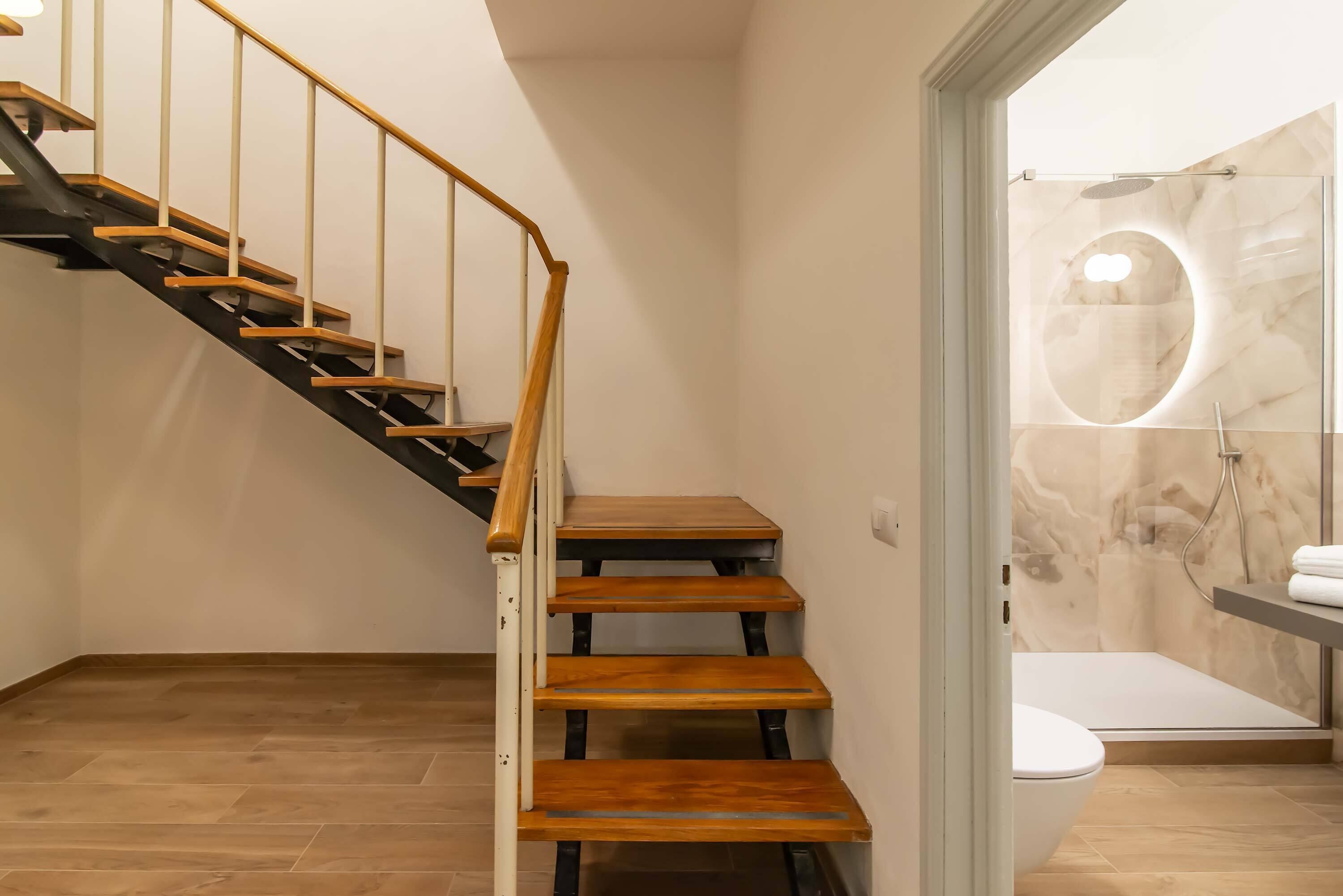 Un escalier avec des marches en bois et des rampes en métal menant à une salle de bain dont un mur est recouvert de marbre et qui est dotée d’une cabine de douche en verre.