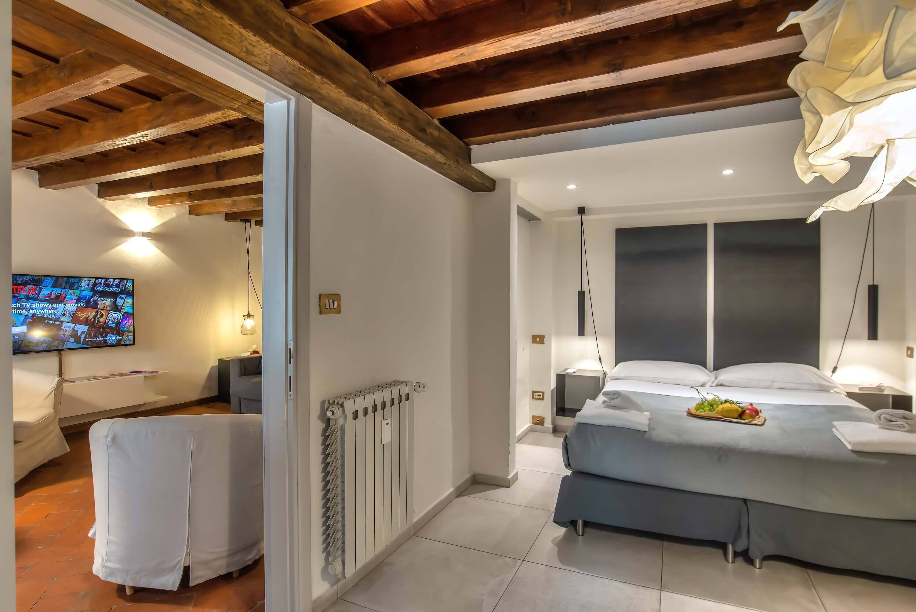 A modern hotel room with a wooden ceiling, a large bed with a blue bedspread, a TV on the left, and a radiator on the wall.