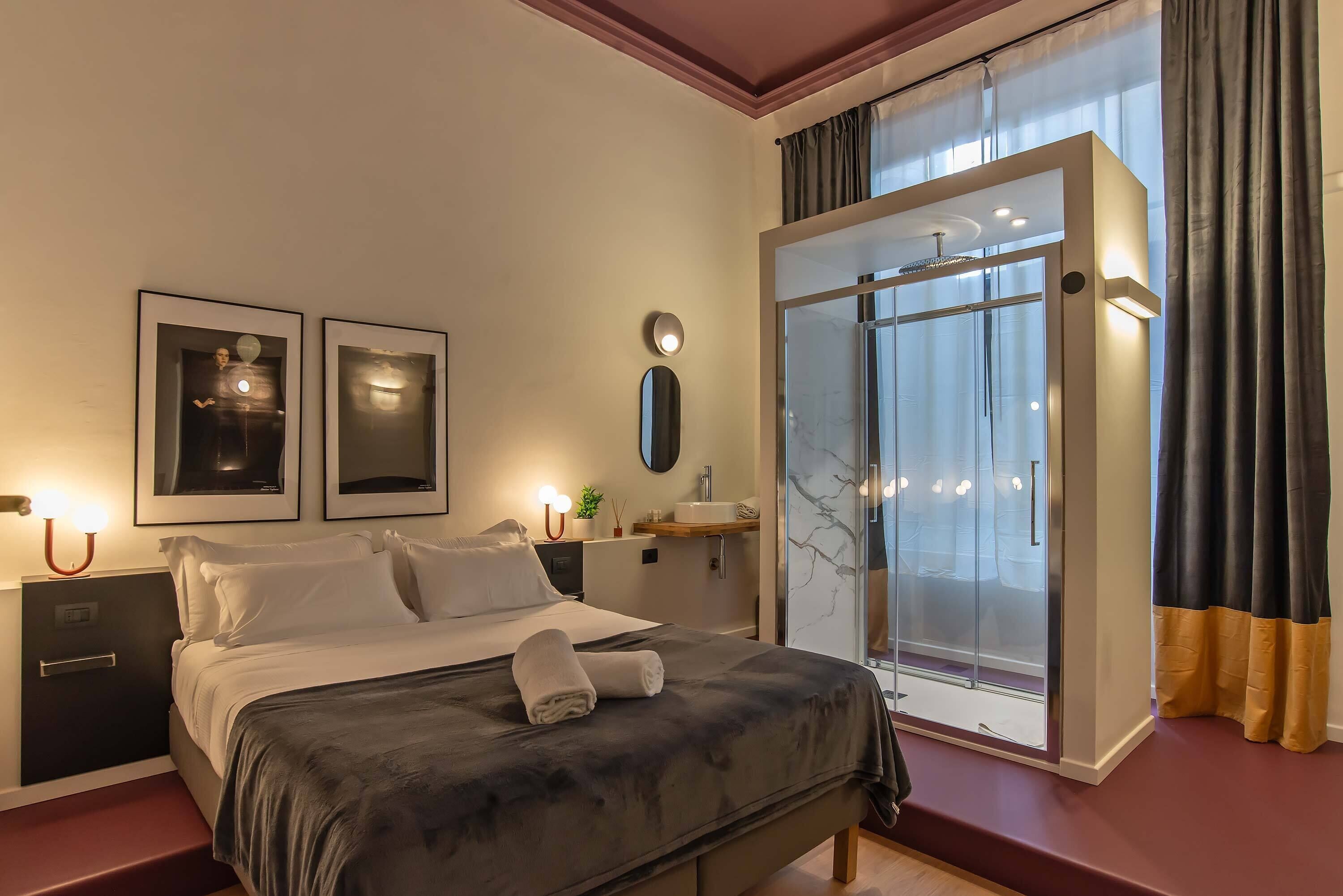 Ein Schlafzimmer mit Bett, Nachttischen, einem Spiegel, einem Fenster mit Vorhängen und einer Duschkabine.