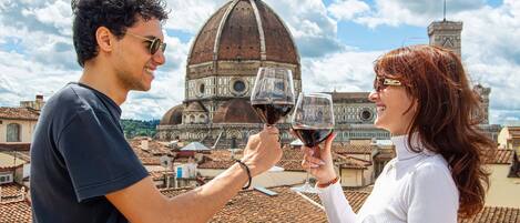 Two people toasting with wine glasses, a domed building in the background, and a clear sky.