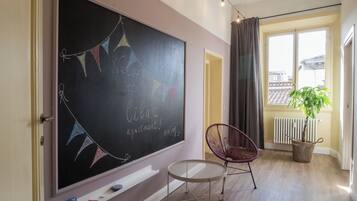 Une pièce comprenant un tableau noir, une chaise, une petite table, une fenêtre avec des rideaux et un radiateur.
