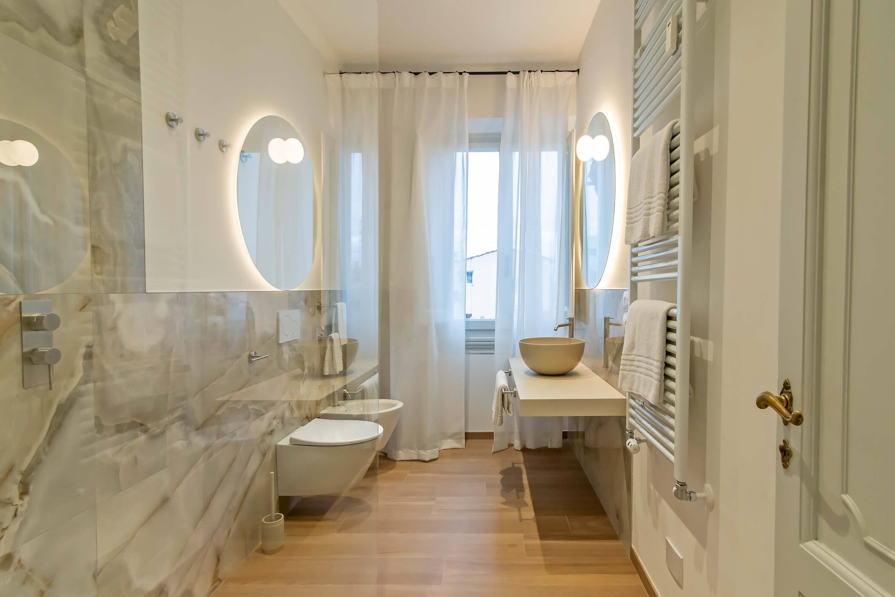 Un baño moderno con pared de mármol, una bañera independiente, un inodoro, un lavabo con un recipiente grande y un perchero para toallas.