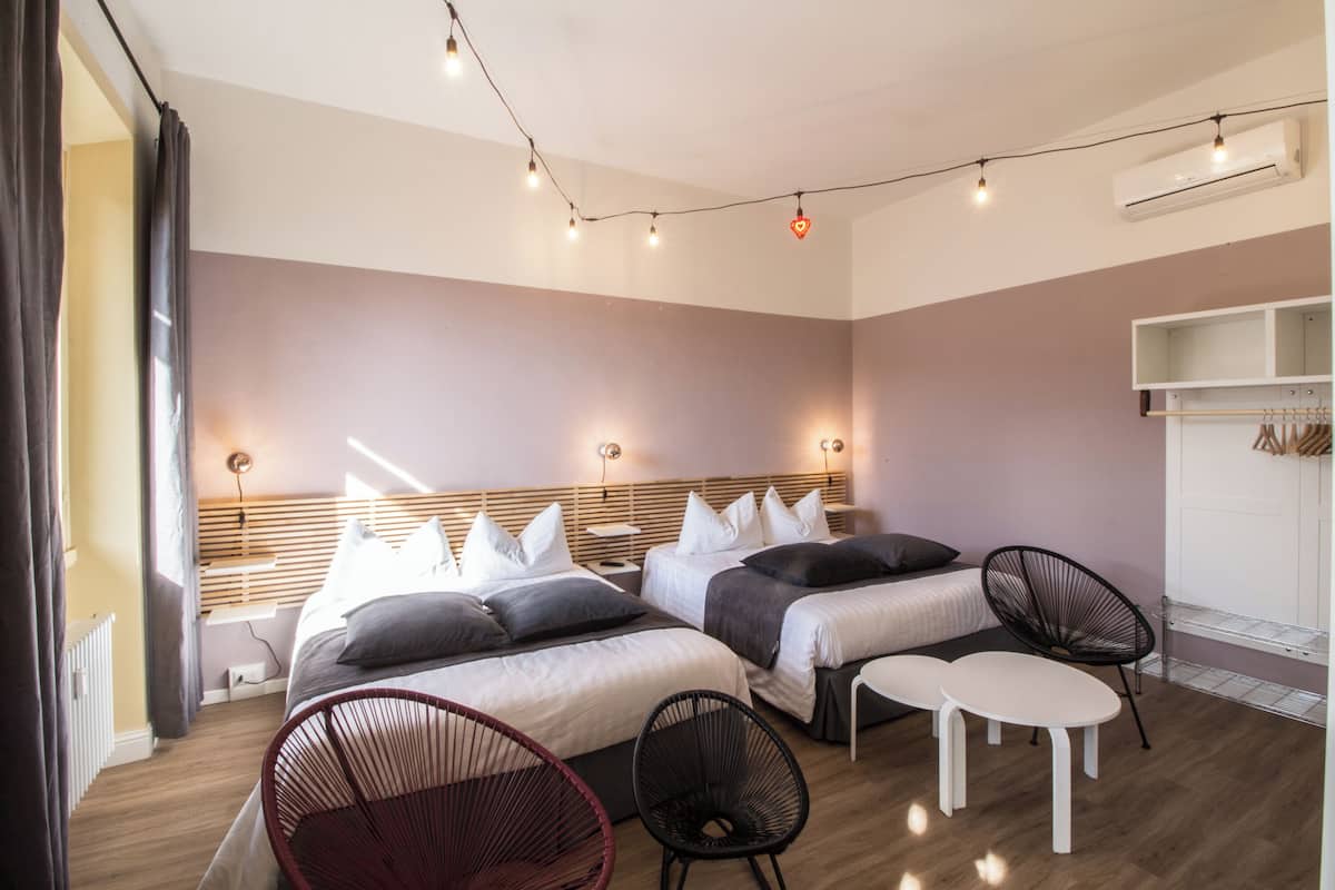 A modern hotel room with two beds, a seating area, and a wardrobe.