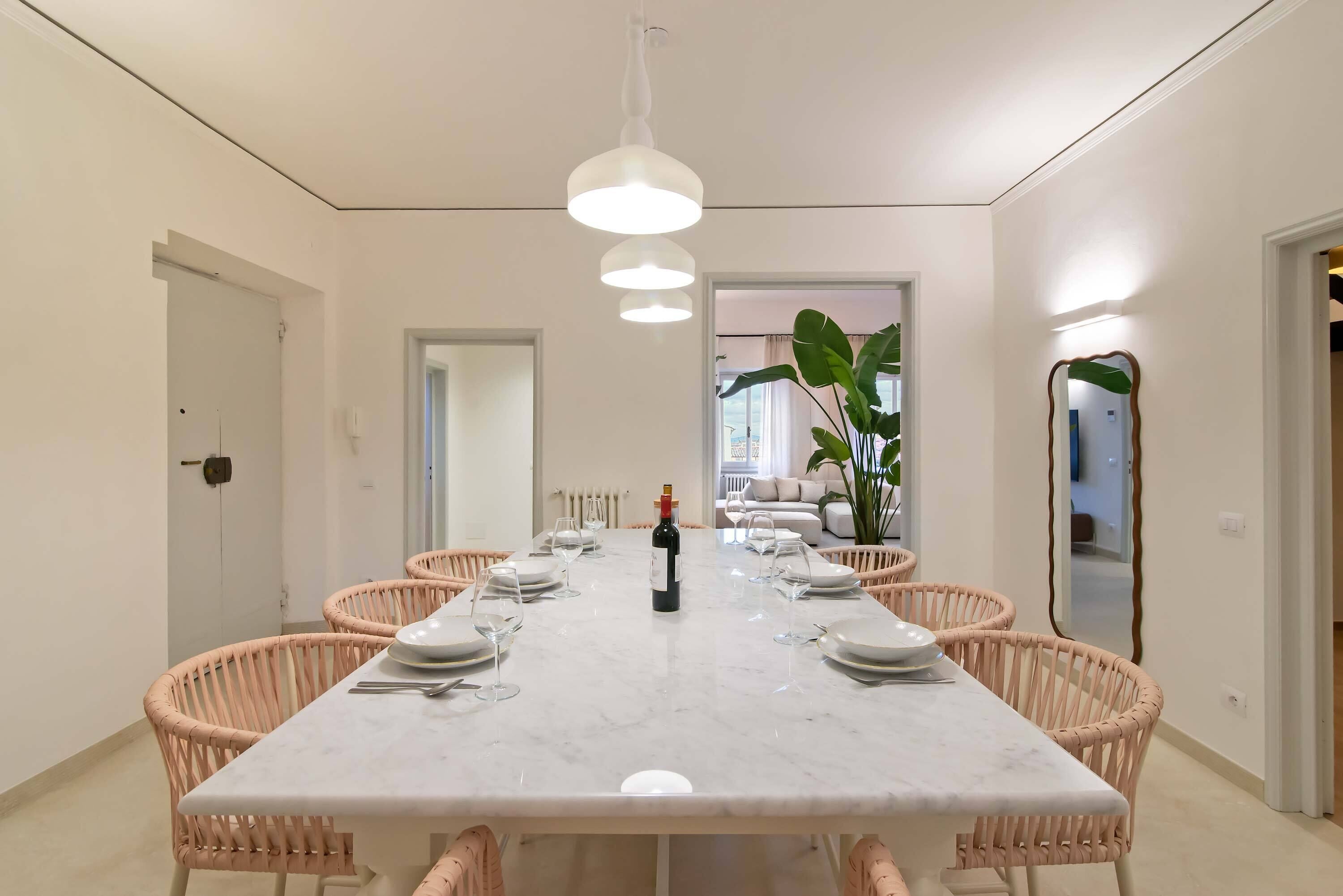A dining room with a marble table, pink wicker chairs, and a wine bottle.
