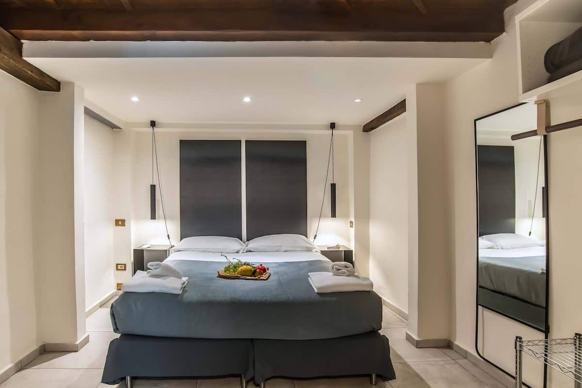 A modern hotel room with a large bed, bedside tables, a mirror, and a fruit basket.