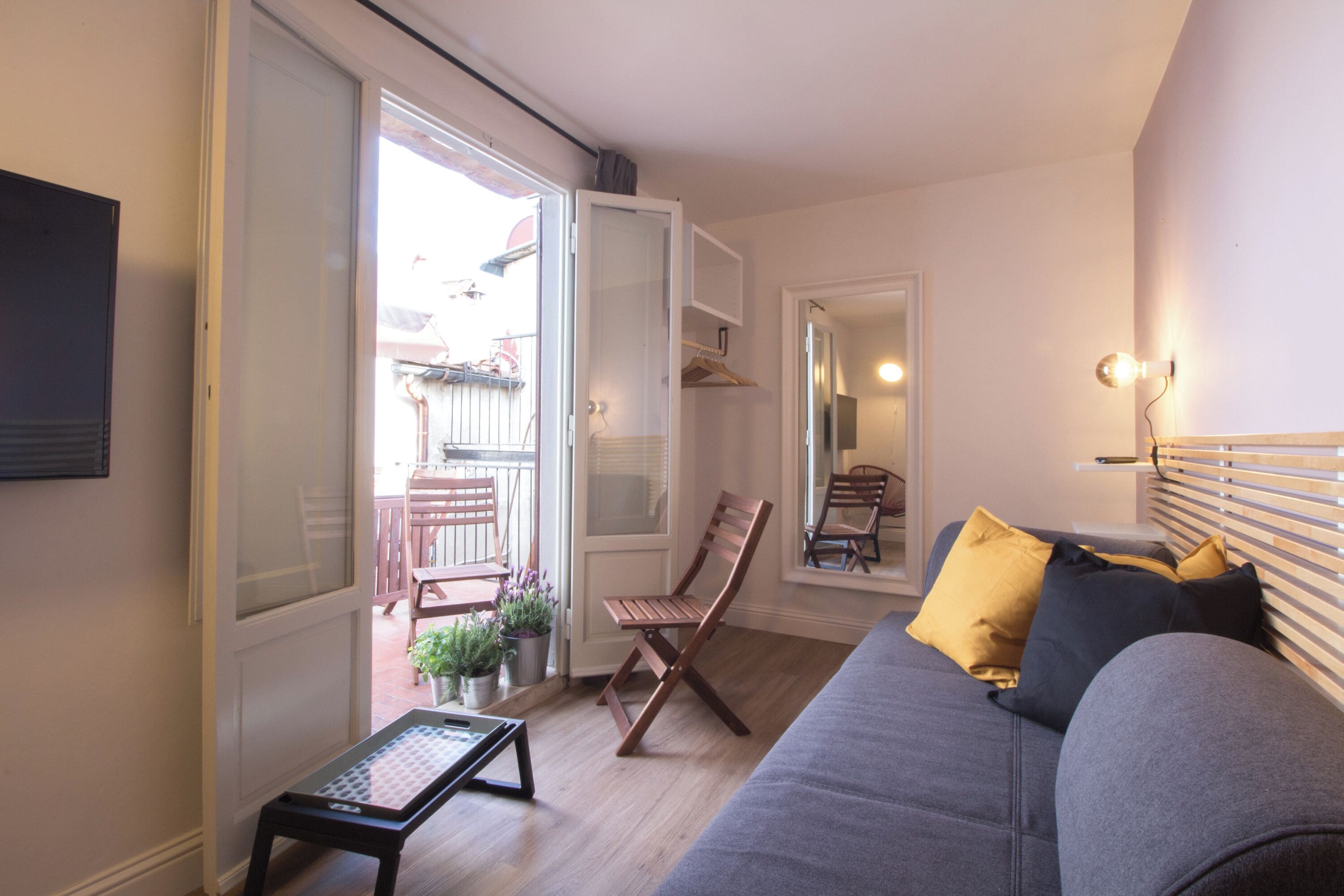 Un salon comprenant un canapé, une chaise en bois, une petite table et une porte-fenêtre coulissante donnant sur un espace extérieur avec une table et des chaises.