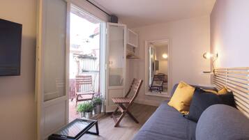 Un salon comprenant un canapé, une chaise en bois, une petite table et une porte-fenêtre coulissante donnant sur un espace extérieur avec une table et des chaises.