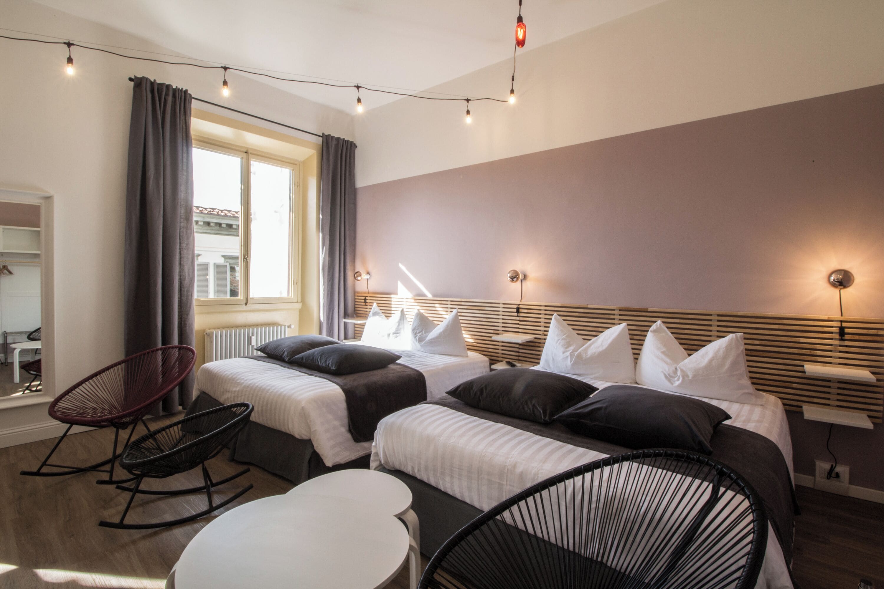 Habitación de hotel con dos camas, una mesita, una silla y una ventana con cortinas.