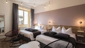 Habitación de hotel con dos camas, una mesita, una silla y una ventana con cortinas.