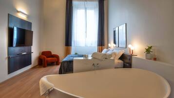 Una habitación de hotel moderna con una bañera grande, un televisor de pantalla plana montado en la pared, un sillón cómodo y una cama con ropa de cama impecable.