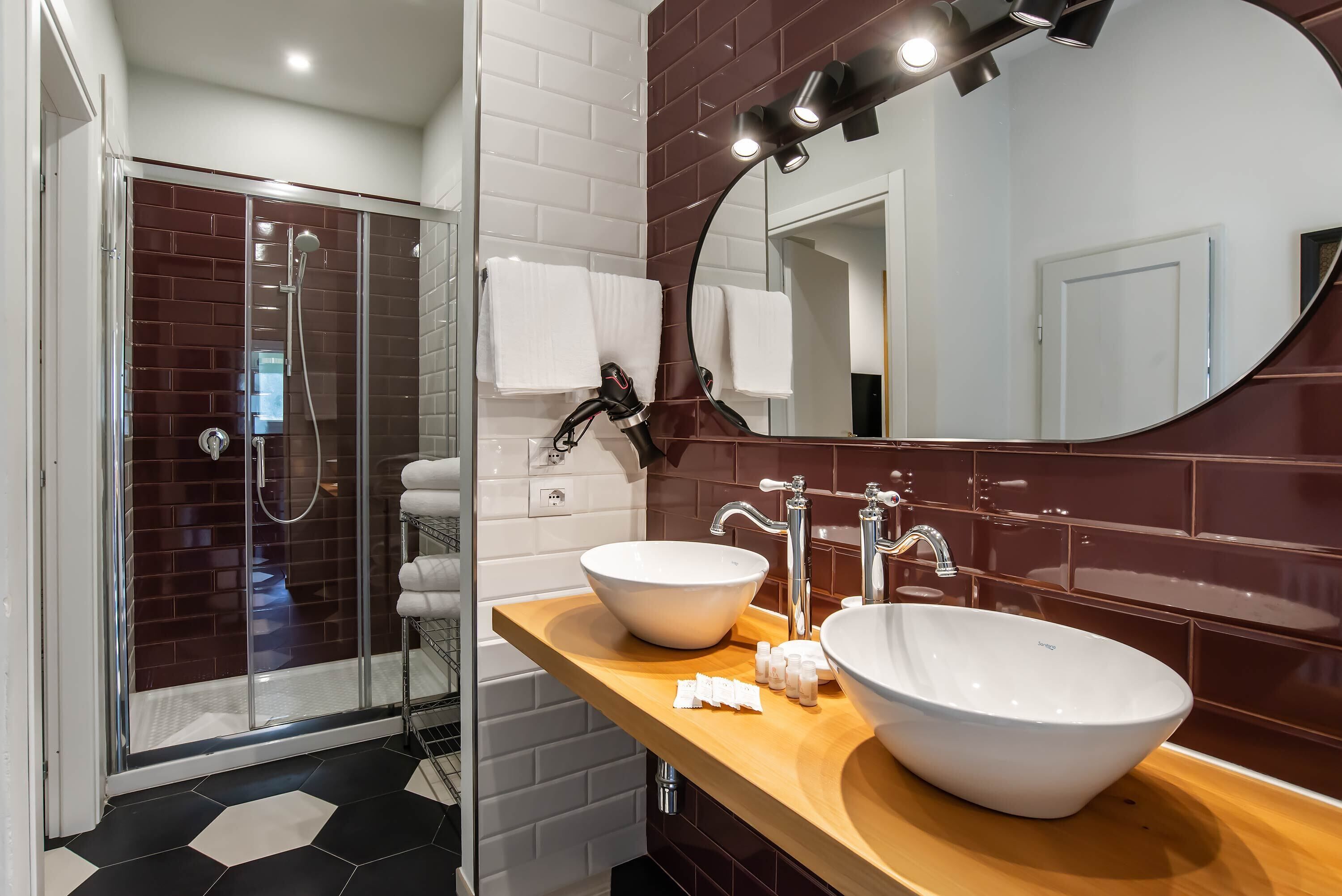 Un baño moderno con cabina de ducha de vidrio, tocador de madera con lavamanos grande y espejo con iluminación.