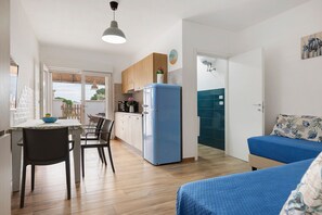 Un espacio habitable compacto con kitchenette, zona de comedor y área de estar con un sofá azul.