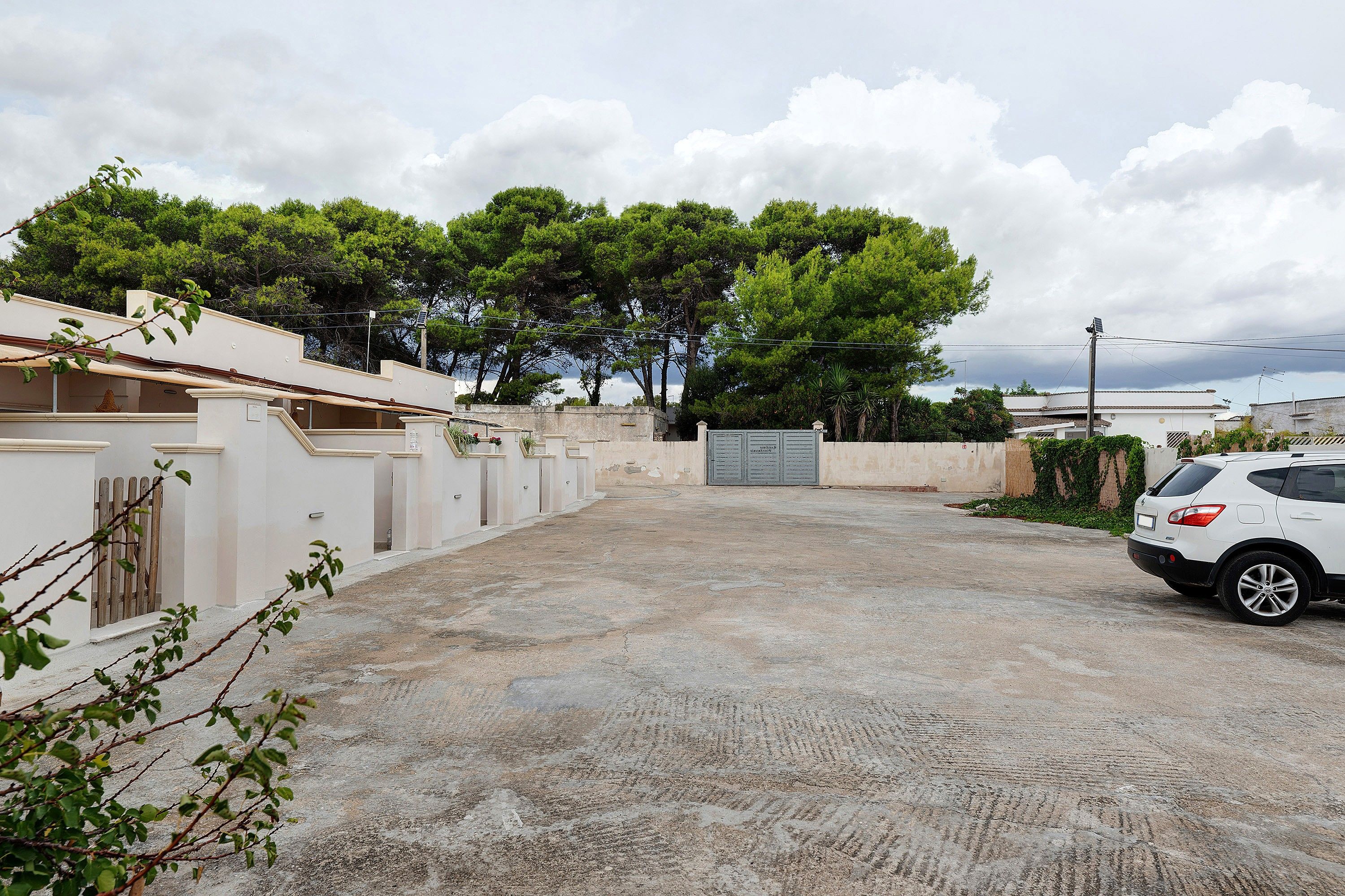 A residential area with a paved driveway, a white car parked on the right, and a gated entrance.