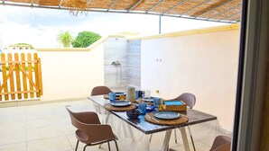 Patio esterno con tavolo apparecchiato per mangiare, sedie, una recinzione di legno e un muro con doccia integrata.
