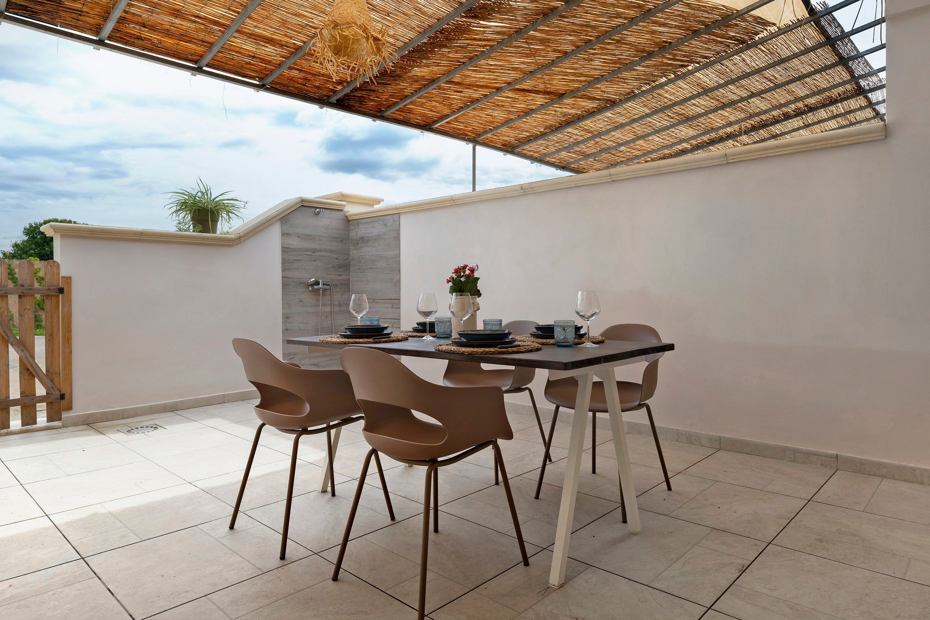 An outdoor patio with a table set for dining, surrounded by chairs, and a pergola overhead.