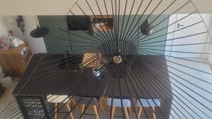 Et spiseområde med et sort bord og stole, et centralt lysarmatur og en grøn rumdeler.
