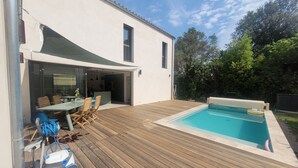 Et moderne hus med en træterrasse, swimmingpool og et spiseområde med udendørs møbler.