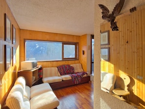 Ein gemütliches Blockhaus-Interieur mit Holzausstattung, einer Couch, einem Sessel und einem kleinen Tisch mit einer Mikrowelle.