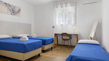 Ein Zimmer mit zwei Betten, einem Schreibtisch, einem Stuhl und einem Fenster mit Vorhängen.