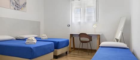 A room with two beds, a desk, a chair, and a window with curtains.