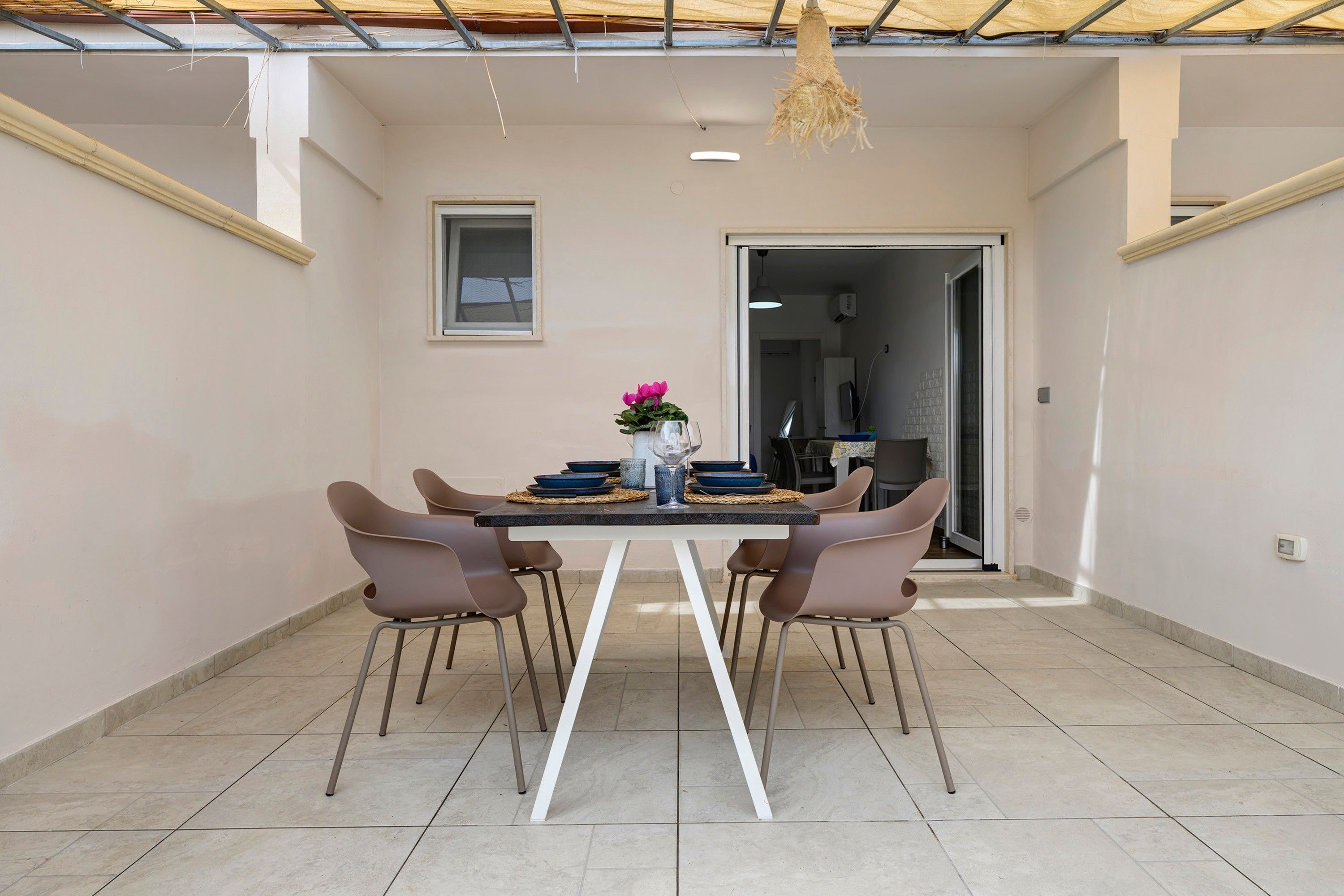 Área de jantar com mesa posta para quatro pessoas, rodeada por cadeiras, e um lustre pendurado acima.